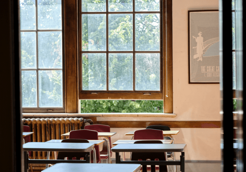 Empty classroom with rows of desks and an open window looking out on green trees